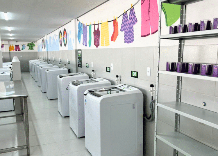 Fileira de máquinas de lavar em lavanderia pública, ilustrando o apoio do governo para reduzir a sobrecarga de trabalho feminino.