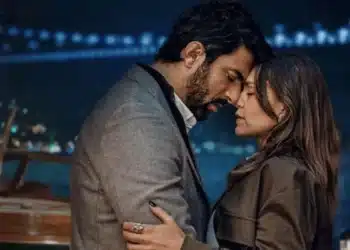 Cena intensa de romance e drama entre dois personagens em uma cidade iluminada à noite, da novela turca 'Berço de Ouro.