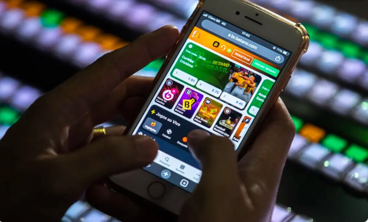 Imagem de celular exibindo a plataforma de apostas Betano com foco em um jogo, com o tema do governo proibindo depósitos em contas BETs para beneficiários do Bolsa Família e BPC.