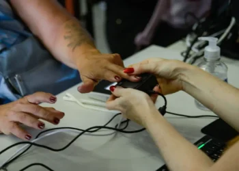 Mãos femininas utilizando oxímetro de dedo para medir batimentos e oxigenação no sangue em uma mesa com álcool em gel.