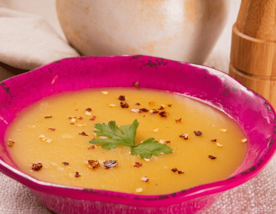 Sopa cremosa amarela em tigela rosa com folhas de salsa e pimenta vermelha triturada