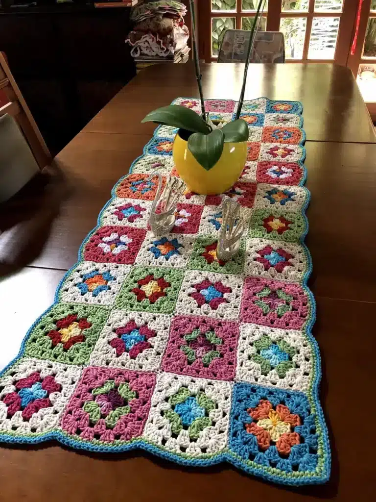 Caminho de mesa com squares coloridos e flores crochetadas, perfeito para decorar a mesa com sobras de fios.