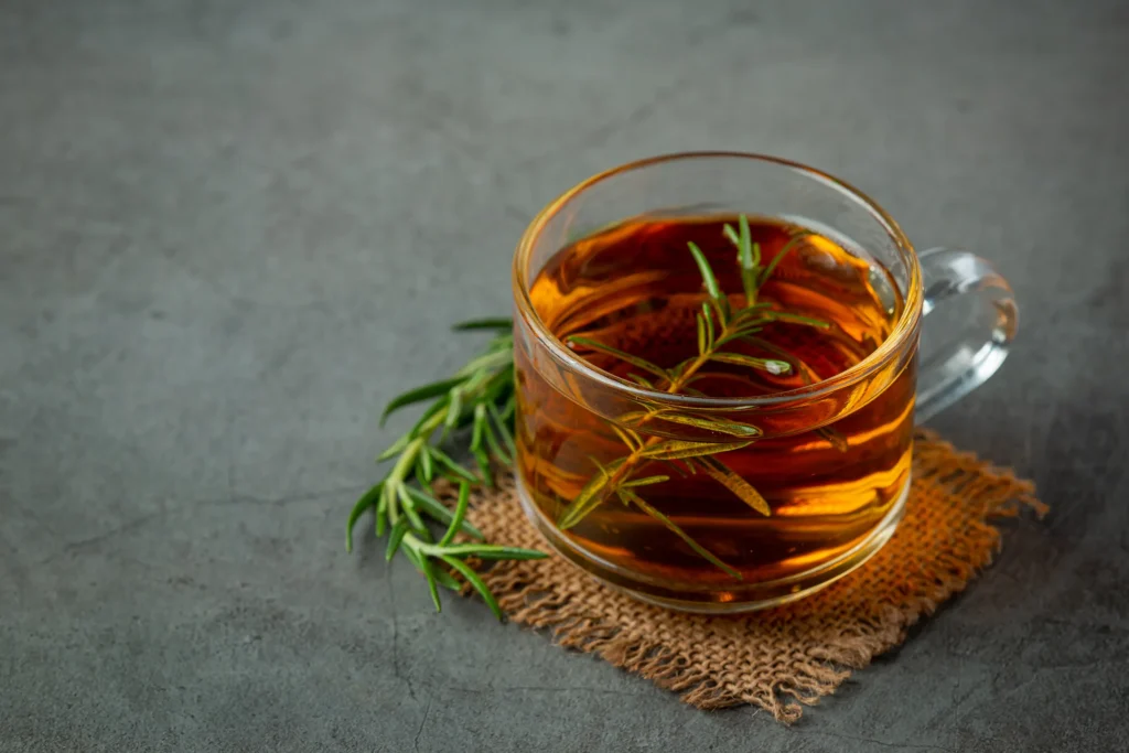 Chá de alecrim em uma xícara transparente com ramos frescos de alecrim, ideal para ajudar na digestão e redução do inchaço.