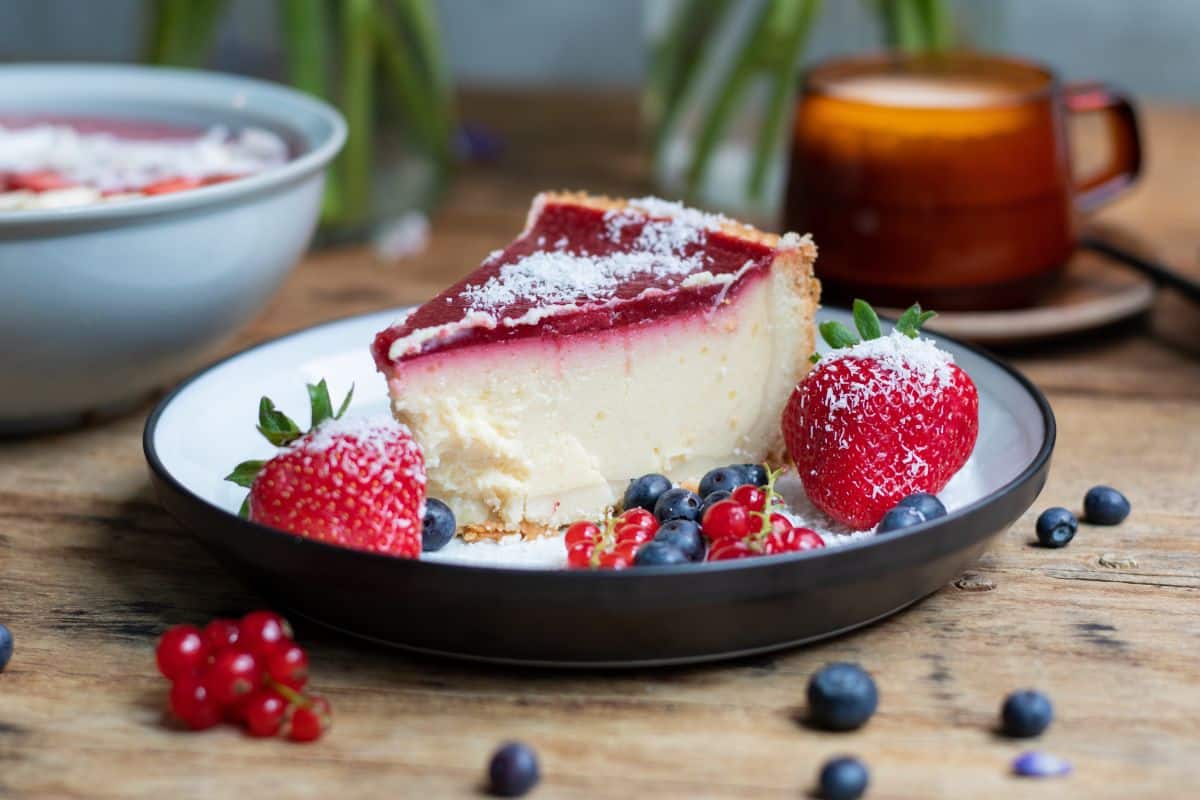 Fatia de cheesecake com calda de frutas vermelhas e morangos, representando uma receita de sobremesa com morangos.
