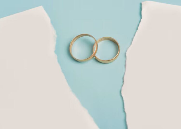 Anéis de casamento sobre papel rasgado, simbolizando o impacto de mudanças na partilha após a morte durante um divórcio.