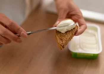 Pessoa espalhando cream cheese caseiro com iogurte natural sobre uma fatia de pão.