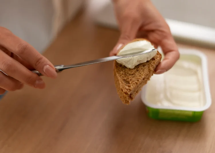 Pessoa espalhando cream cheese caseiro com iogurte natural sobre uma fatia de pão.