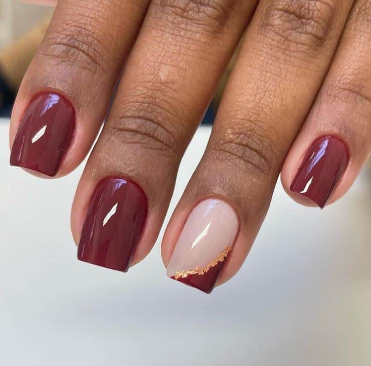 Unhas com esmalte na cor marsala (vinho escuro) e uma unha decorada em tom nude com detalhes em ouro. Representa uma tendência moderna da variação do vermelho.