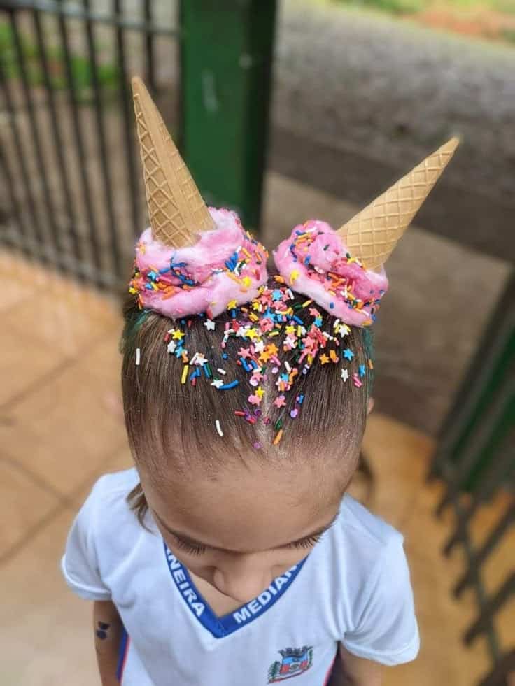Cabelo maluco estilo sorvete em criança, com dois coques altos coloridos de rosa, granulados coloridos e cones de biscoito.