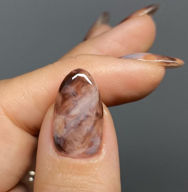 Unha do polegar com esmalte em efeito mármore nas cores marrom, nude e branco, ideal para um visual elegante.