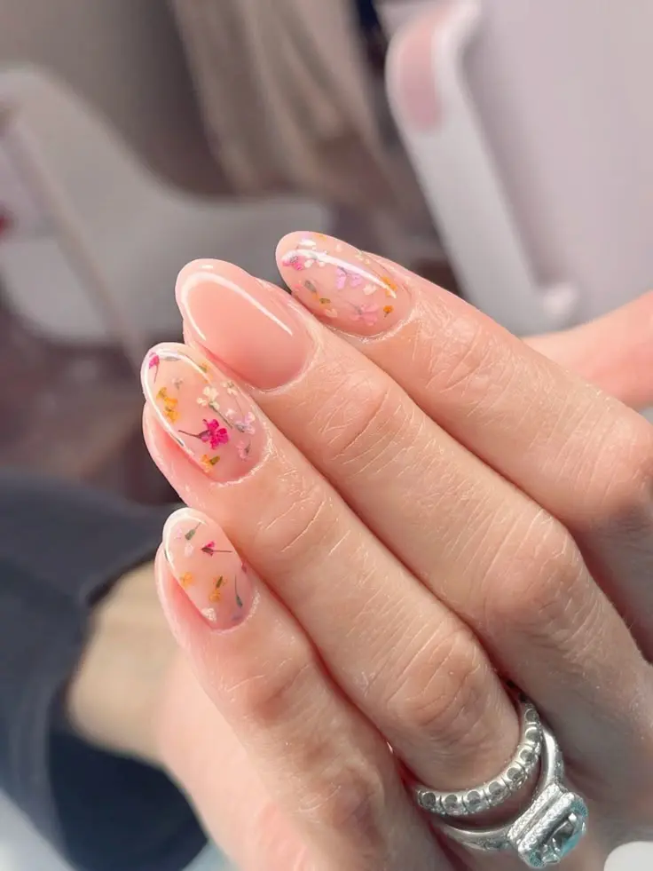 Unhas em formato amendoado com flores secas encapsuladas em gel, criando efeito 3D delicado.