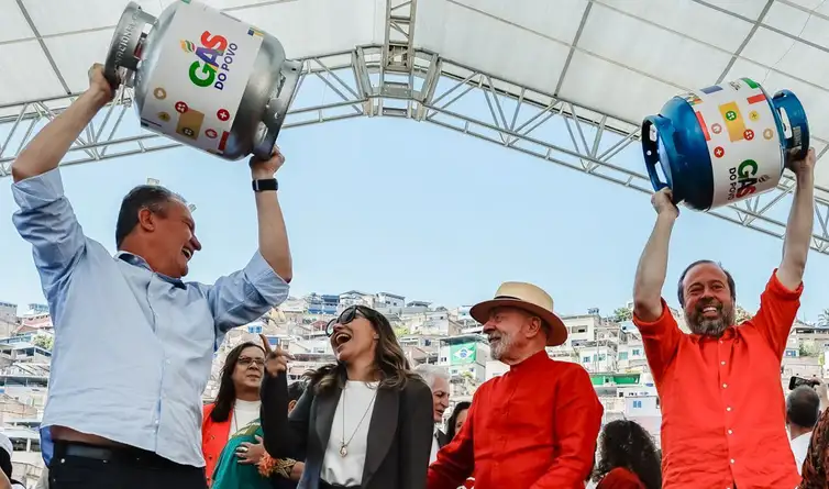 Pessoas celebrando lançamento do programa Gás do Povo com botijões de gás coloridos em evento ao ar livre