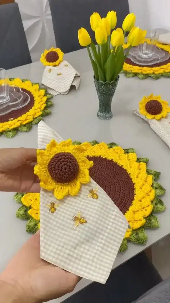 Girassóis de crochê decorando uma mesa com toalha de linho e flores amarelas.