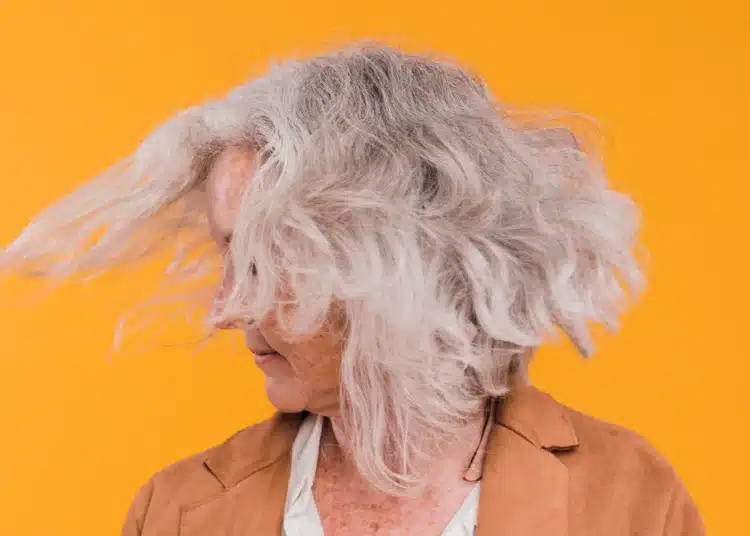 Mulher com cabelo grisalho e volumoso, mostrando movimento com o vento.