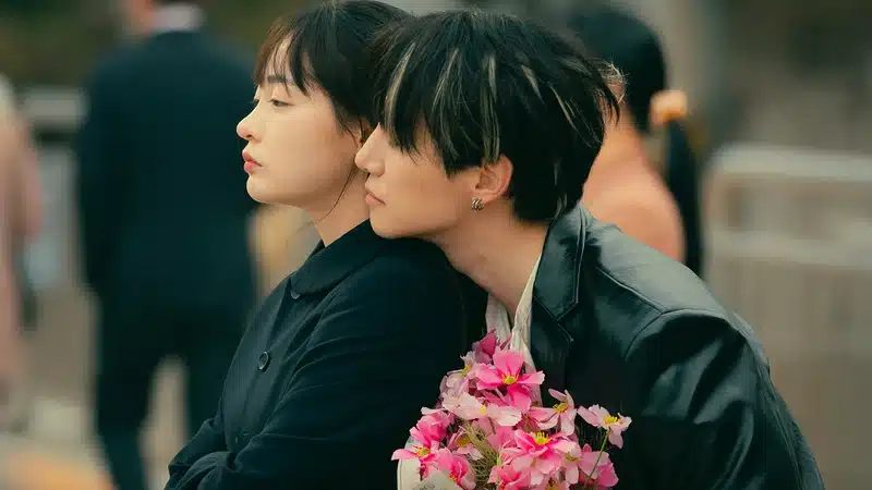 Casal jovem se abraçando em um momento de ternura na cidade, com um buquê de flores cor-de-rosa. A cena ilustra o drama e o romance do novo dorama "Typhoon Family" que estreia em outubro.