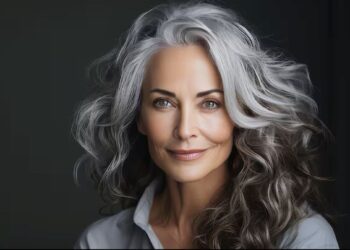 Mulher madura com cabelos grisalhos longos e ondulados, sorrindo, representando um visual rejuvenescido.