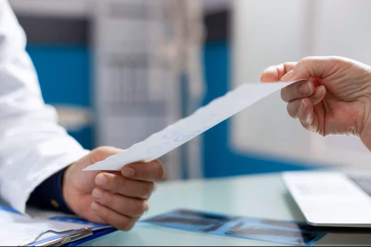 Mãos de um profissional de saúde (jaleco branco) entregando uma receita médica ou documento a um paciente. Foco na transferência da prescrição.