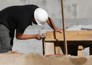 Homem usando capacete branco ajustando estrutura de madeira em obra de construção civil