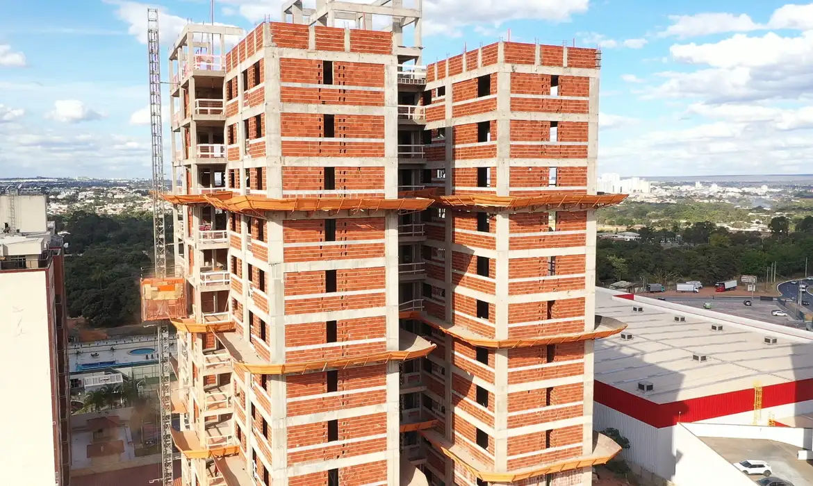 Prédio de apartamentos em construção com paredes de tijolos e estrutura de concreto à vista em área urbana.
