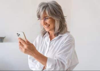 Mulher sorrindo e interagindo alegremente com um smartphone, demonstrando facilidade e satisfação ao usar o aparelho.