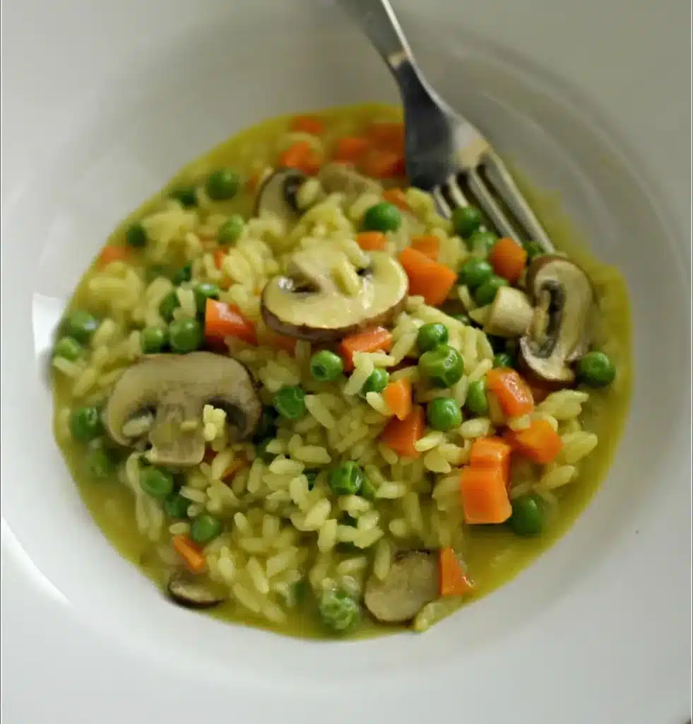 Risoto primavera com legumes frescos coloridos servido em prato branco.