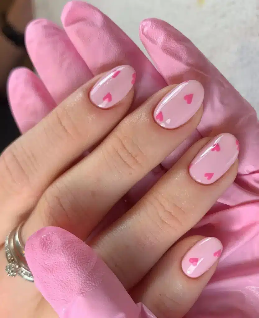 Unhas minimalistas com base rosa e detalhes delicados de cor pink, incluindo pequenos corações.