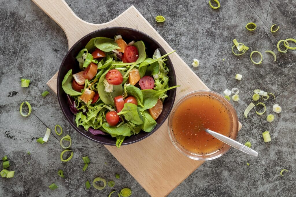 Vista superior de uma salada fresca com fatias de laranja e tomate, ao lado de uma tigela de molho caseiro.