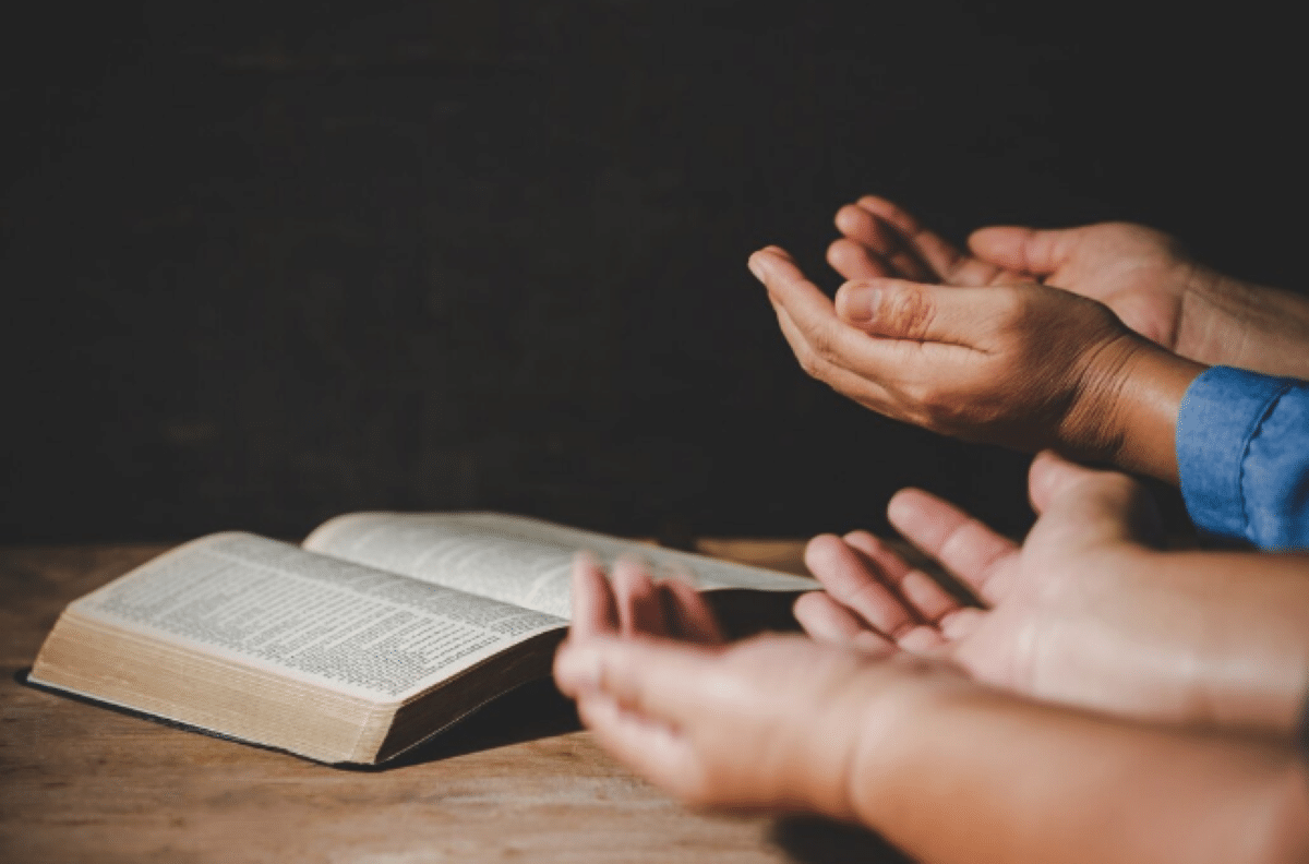 Pessoas rezando com bíblia aberta na mesa