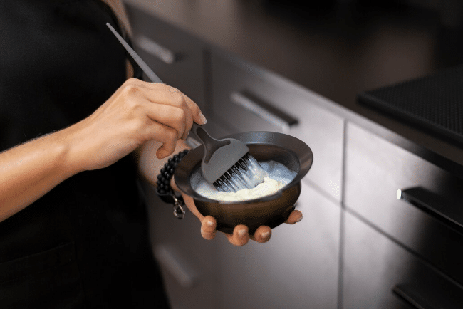 Mãos segurando tigela com tintura e pincel aplicador em ambiente profissional