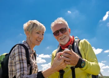 Casal de idosos sorrindo enquanto exploram a natureza, verificando equipamento em uma caminhada ao ar livre em um destino de viagem tranquilo.