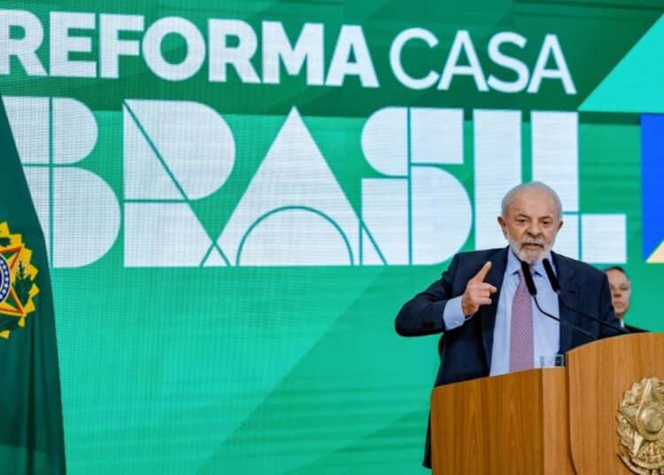 O Presidente da República, Lula, em um discurso oficial, apontando para o painel de fundo com a inscrição "REFORMA CASA BRASIL". A imagem marca o lançamento deste novo programa de habitação e melhoria residencial do governo.