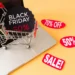 Carrinho de compras sobre um notebook com anúncios de descontos da Black Friday 2025.