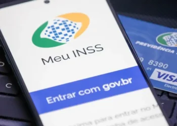 Celular exibindo tela do app Meu INSS com cartão da Previdência Social sobre teclado.
