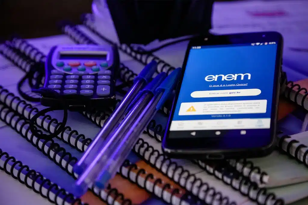 Imagem mostrando materiais de estudo como calculadora, canetas e celular com aplicativo ENEM aberto.