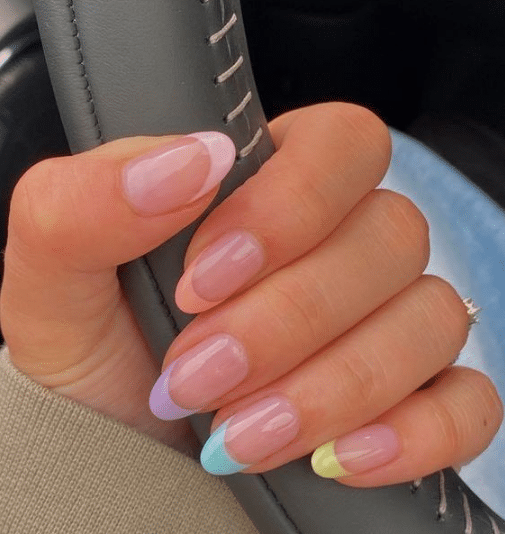 Mão segurando volante com unhas delicadas em pontas coloridas rosa, lilás, azul, verde e amarelo pastel