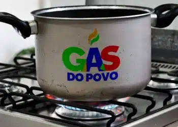 Panela no fogão com chama acesa exibindo o logo “Gás do Povo”, relacionado ao fim do Auxílio Gás e às novas regras do programa.