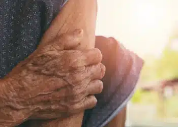 Mãos enrugadas de um idoso segurando o braço de outra pessoa em gesto de apoio e cuidado