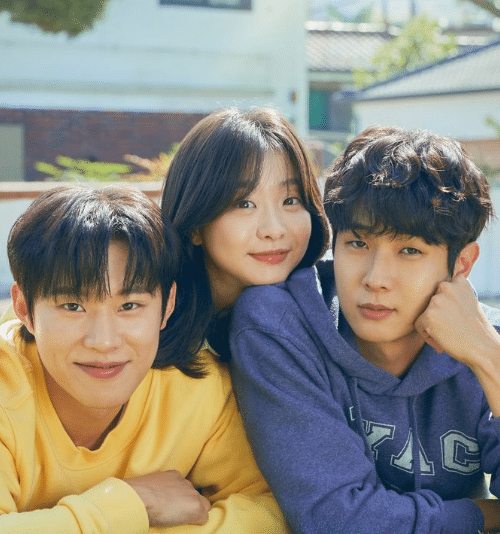 Dois homens e uma mulher jovens sorrindo, o homem à esquerda veste moletom amarelo e o outro azul, próximos em cenário externo