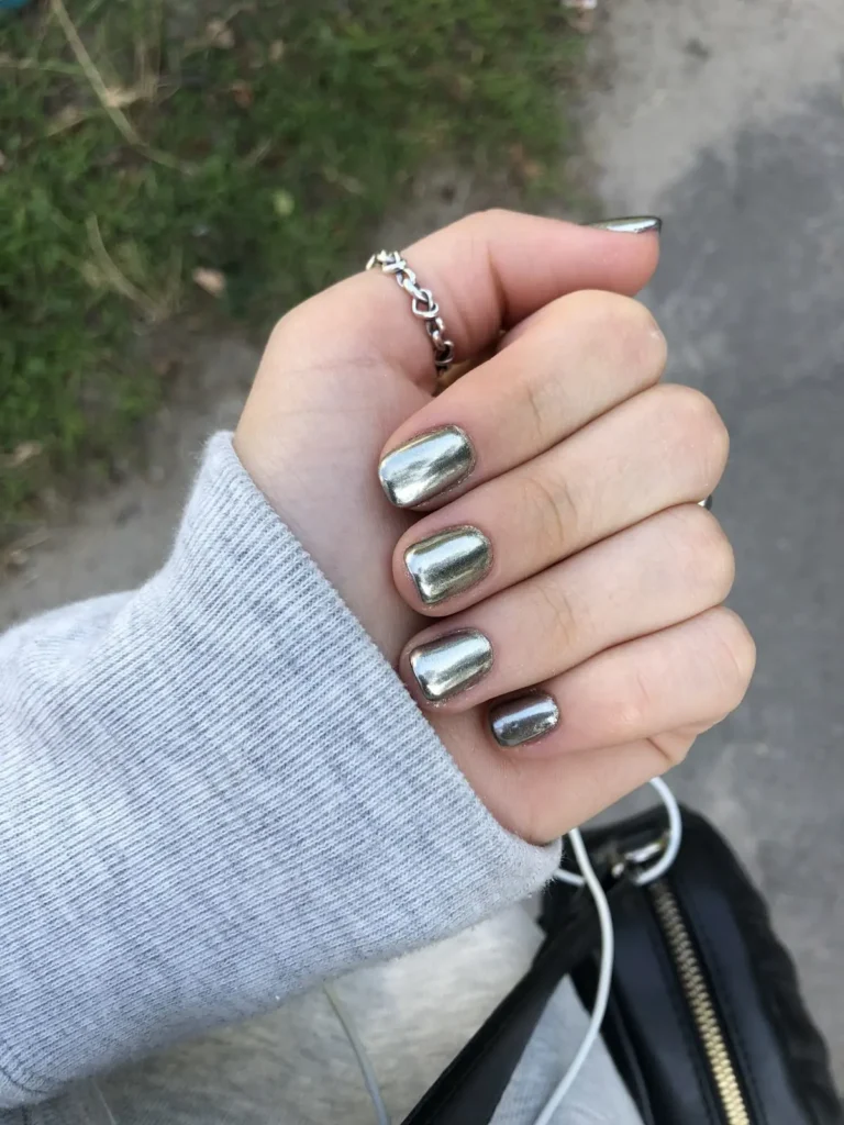 Unhas com esmalte cromado prateado espelhado, refletindo a luz com acabamento metálico moderno.