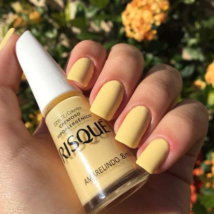 Esmalte cremoso Risqué Amarelindo, em um tom de amarelo manteiga, aplicado nas unhas como tendência de cor e moda.