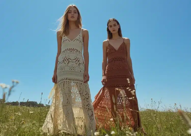 Duas mulheres usando vestidos longos de crochê estilo boho em um campo sob o céu azul.