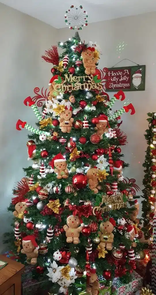 Árvore de Natal decorada com enfeites temáticos, incluindo biscoitos de gengibre, bolas vermelhas e douradas, e flores natalinas.