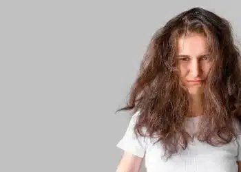 Mulher com cabelo volumoso e embaraçado, mostrando expressão de frustração, ilustrando o impacto do calor no cabelo.