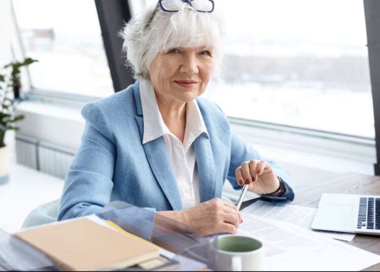 Mulher sênior sorridente em ambiente de trabalho moderno, simbolizando o sucesso na carreira após os 60 anos.