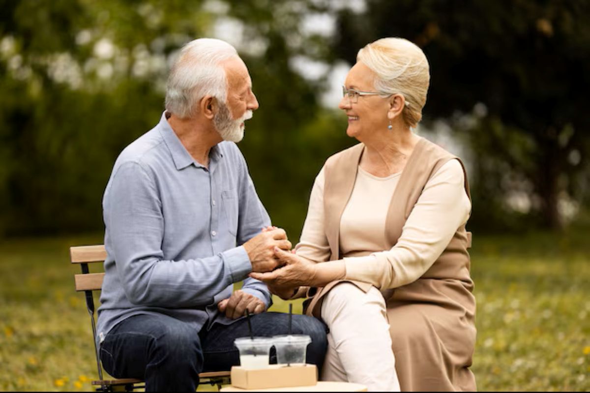Casal idoso sorrindo enquanto conversa e compartilha um momento de carinho ao ar livre