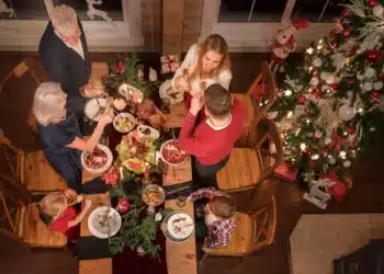 Família reunida em uma mesa de Natal, brindando com taças de champanhe e celebrando com uma ceia deliciosa.