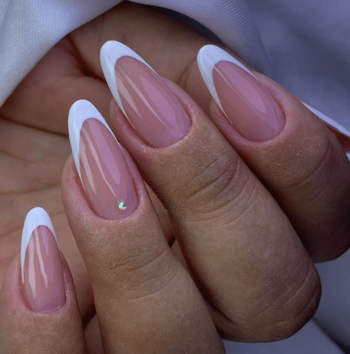 Mãos com unhas stiletto em francesinha branca e esmalte nude, detalhe de strass brilhante
