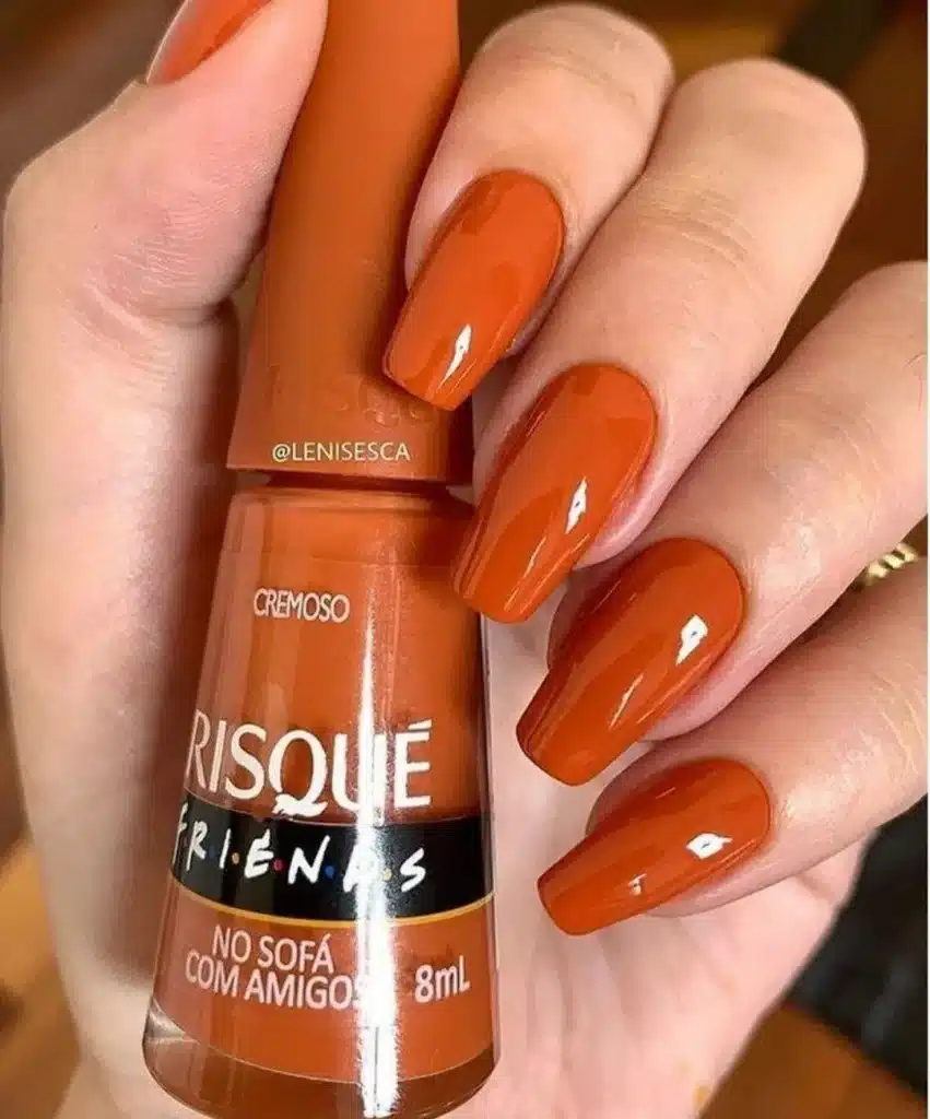 Unhas pintadas com esmalte laranja queimado, trazendo um toque vibrante e terroso.