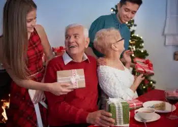 Família reunida durante as festas de Natal, trocando presentes com sorrisos e alegria, perto da árvore de Natal.