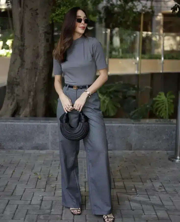 Mulher usando look cinza monocromático com calça pantalona e blusa de manga curta em ambiente urbano.